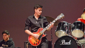 Male student playing the guitar on stage
