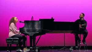 Student singing and playing the piano accompanied by someone playing the guitar
