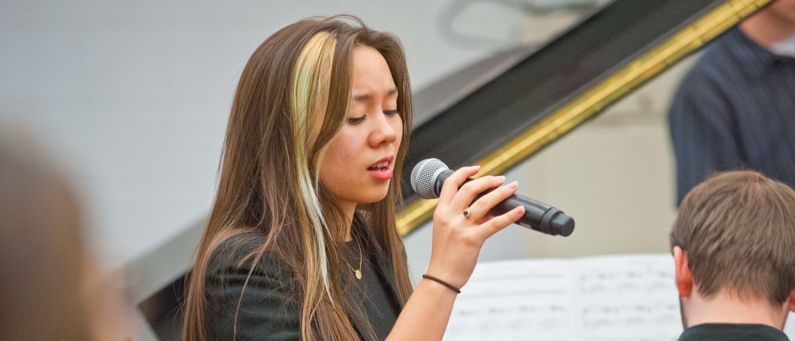 Girl student singing with a microphone in a classroom next to a piano