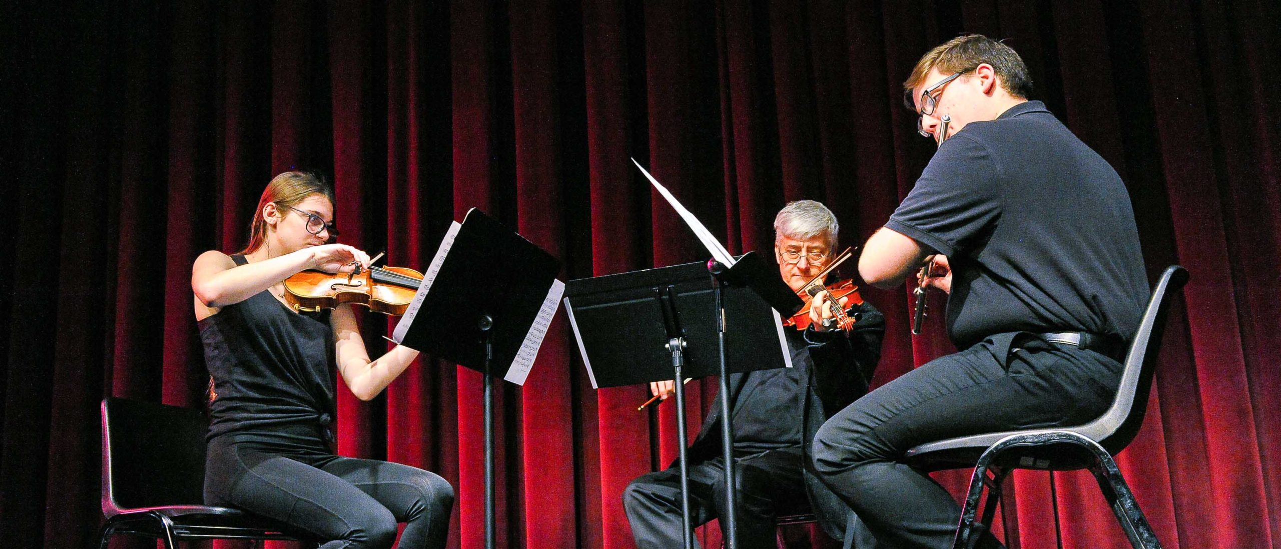 Two students and a faculty member playing string instruments on stage