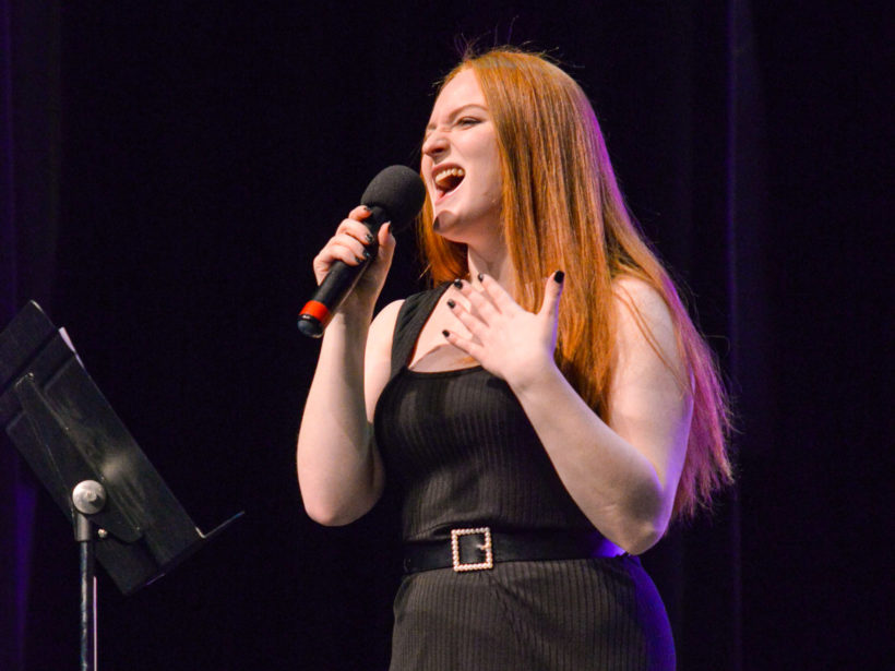 Female student singing on stage with a microphone