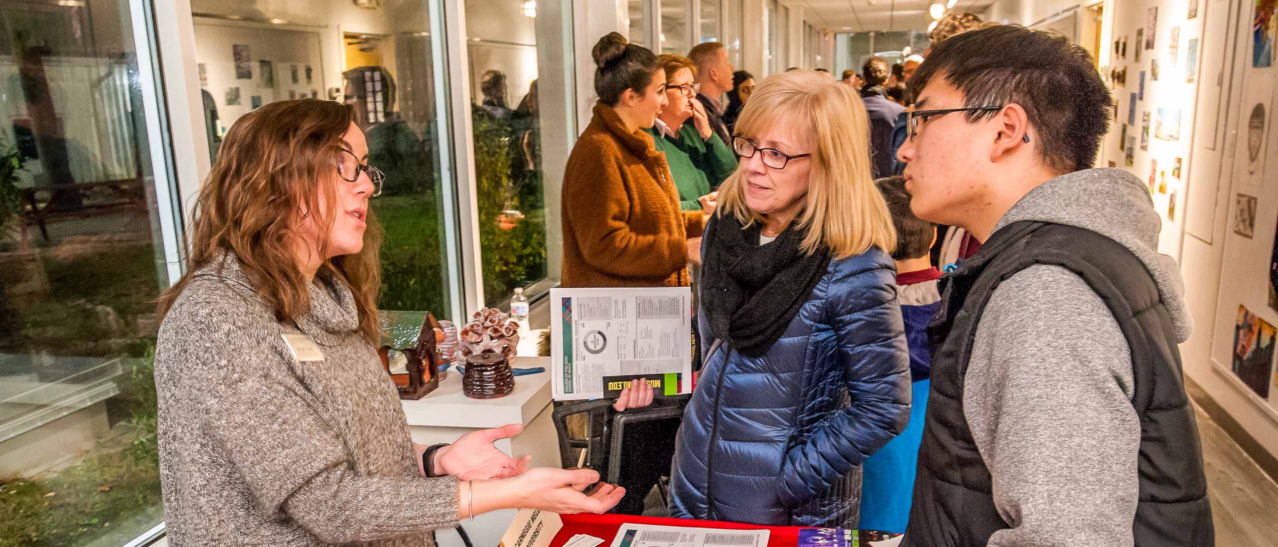 Student and parent talking with someone at a table during a school fair