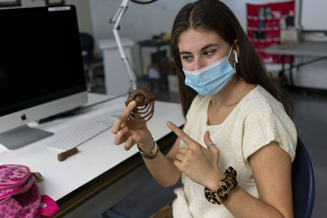 student holding up and pointing at their sculpture